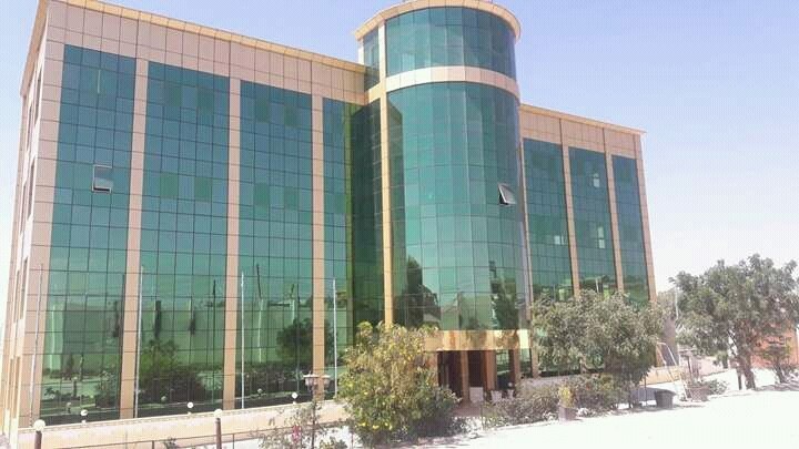 Wide shot of the outside of the hotel showing beautiful teal class windows reflecting the sun with trees and bushes out front